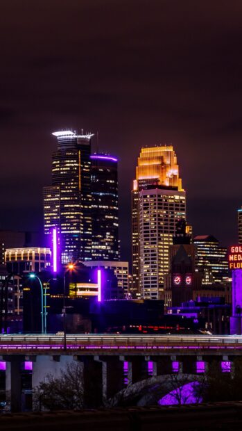 Night cityscape with Minneapolis skyline illuminated by vibrant purple and gold lights
