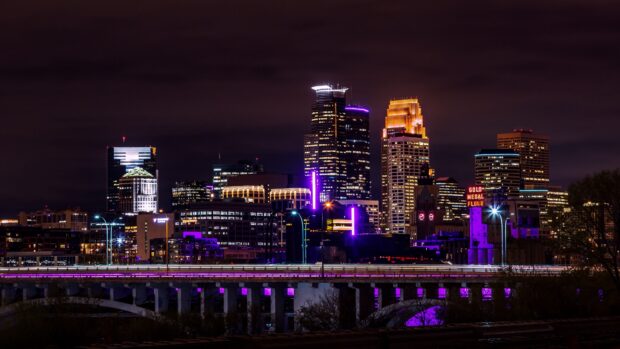 Night view of Minneapolis cityscape with illuminated buildings and purple lights on bridge