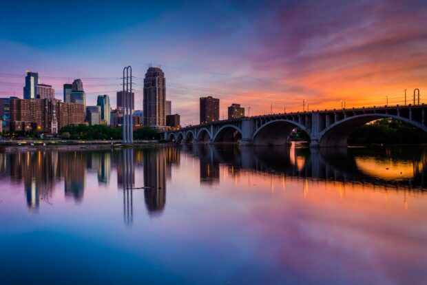 Minneapolis skyline with bridge under colorful sunset sky reflecting on calm water