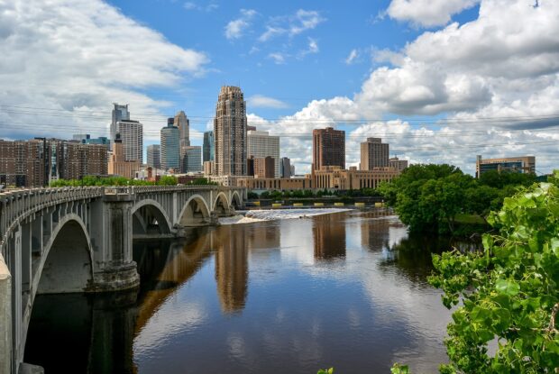 Minneapolis skyline with river and bridge under a bright blue sky