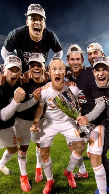 Excited soccer players celebrating their MLS victory with the championship trophy on the field