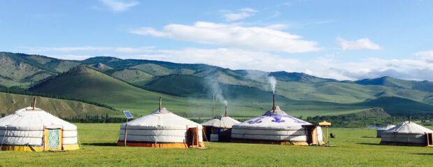 Traditional Mongolian tents in a green valley surrounded by rolling hills and clear sky