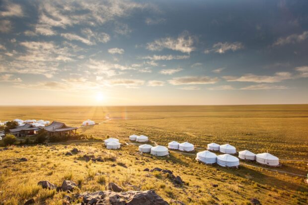 Traditional Mongolian ger tents on grassy hills under a bright sky in Mongolia