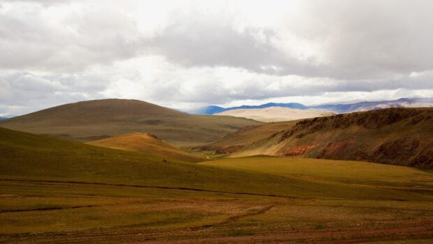 Rolling hills and vast grasslands in Mongolia under a cloudy sky