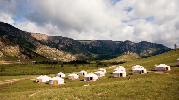Traditional Mongolian tents on a grassy field with mountains in the background