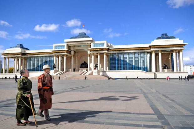 Two elderly people wearing traditional Mongolian clothing walk near the government building in Mongolia