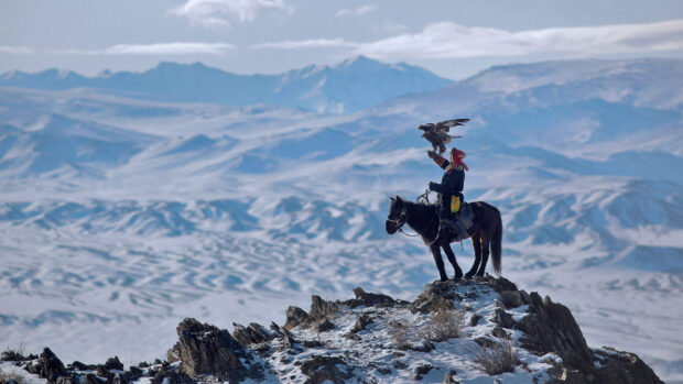 A Mongolian eagle hunter on horseback in the snowy mountains of Mongolia