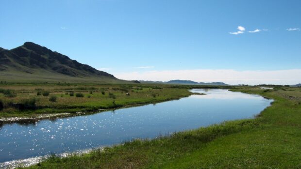 A serene Mongolia landscape with a river flowing through green grasslands and distant mountains under a clear blue sky