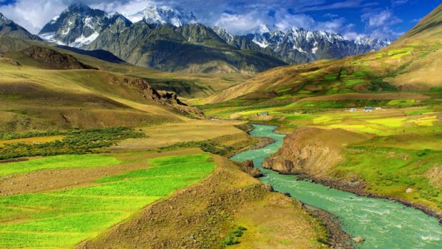 A vibrant Mongolia landscape with snow capped mountains and a flowing river through green fields