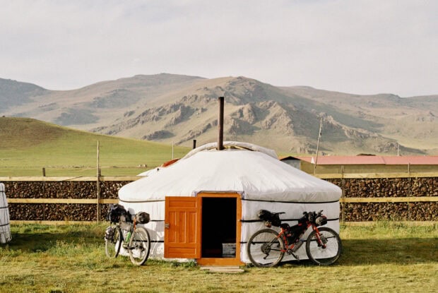 A traditional Mongolian yurt with bicycles parked outside in a grassy landscape