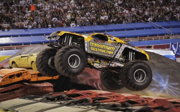 A monster truck performing a high jump over crushed cars in an arena filled with spectators