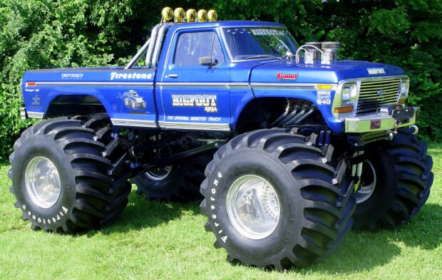 Blue Bigfoot monster truck parked on grass with large tires and decals