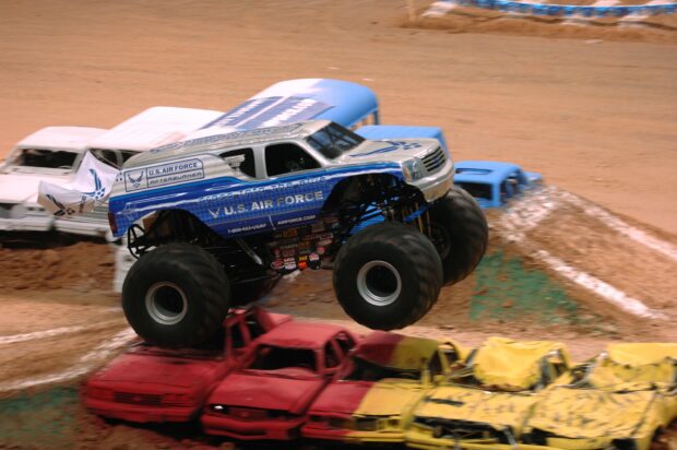 Blue monster truck crushing cars during a dirt race event with U.S Air Force branding