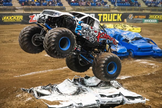 A monster truck crushing cars during a high energy stunt at a live event