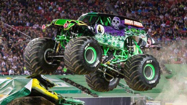 A green monster truck performing a jump during a monster truck event in front of a large crowd