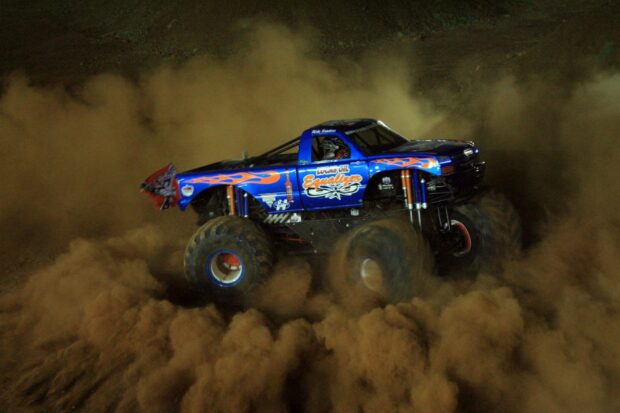 Blue monster truck drifting on dirt track raising dust clouds