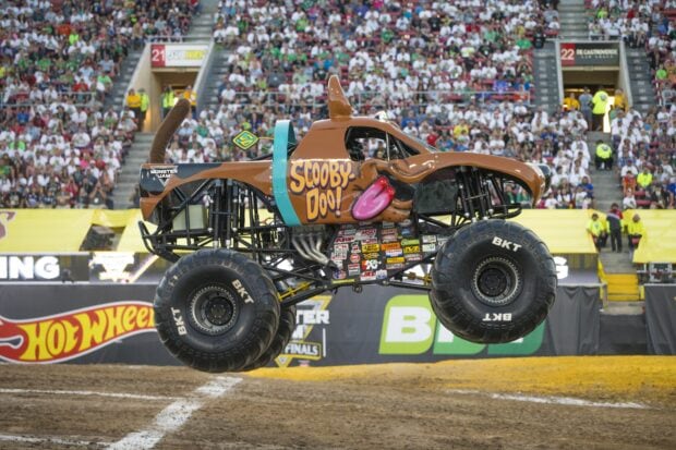 Monster truck designed as Scooby Doo car jumping in stadium crowd