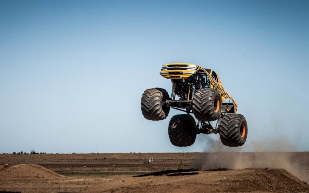 Yellow monster truck jumping high on dirt track in clear sky