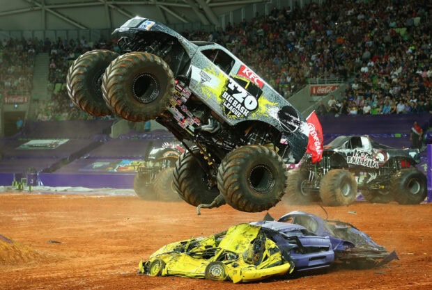 A monster truck jumps over crushed cars during a live monster truck event in a stadium