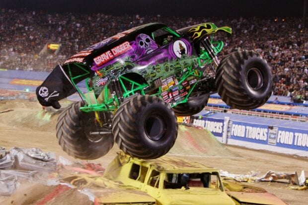 A monster truck performing a jump over crushed cars at a large stadium event