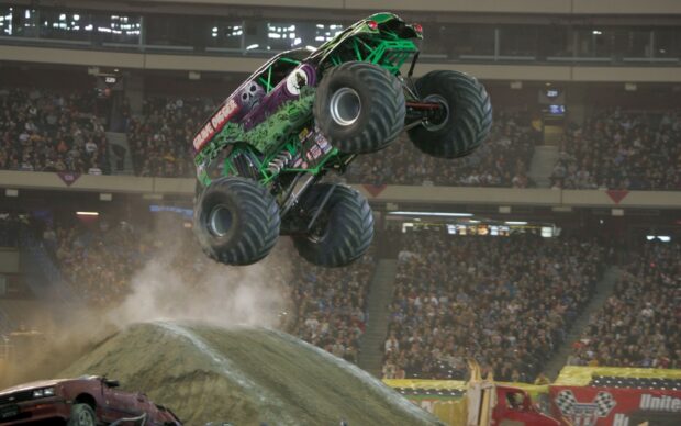 A Grave Digger monster truck jumps over a dirt mound at a stadium event