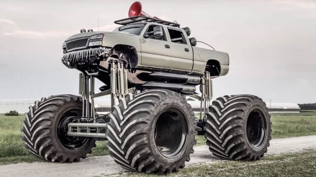 A monster truck with giant tires parked on a dirt road in a grassy field