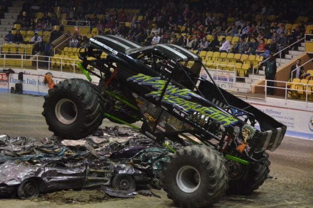 Black insane destructor monster truck crushing cars in arena with crowd watching