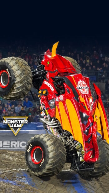Red and orange monster truck performing a wheelie on dirt at a Monster Jam event with a crowd in the background