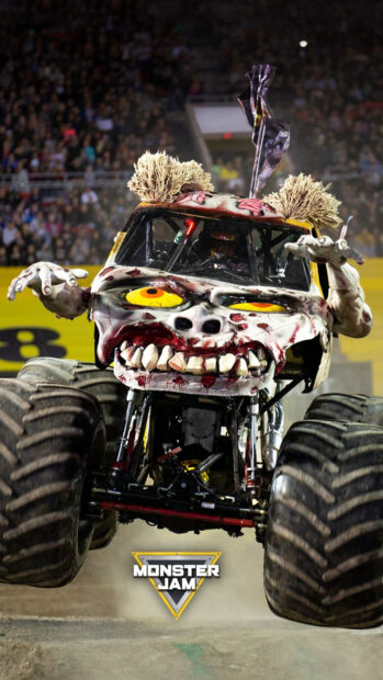 A monster truck with a scary face design performs a jump at a crowded Monster Jam event