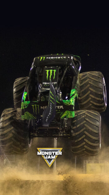 Monster truck with Monster Energy logo jumping over dirt at night