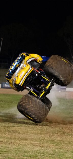 A monster truck performing a wheelie on a dirt field under night sky