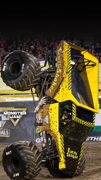 Yellow EarthShaker monster truck performing a wheelie stunt in a crowded arena