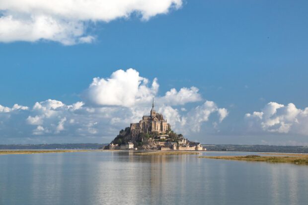 Mont Saint Michel island with historic buildings surrounded by water under a blue sky with clouds