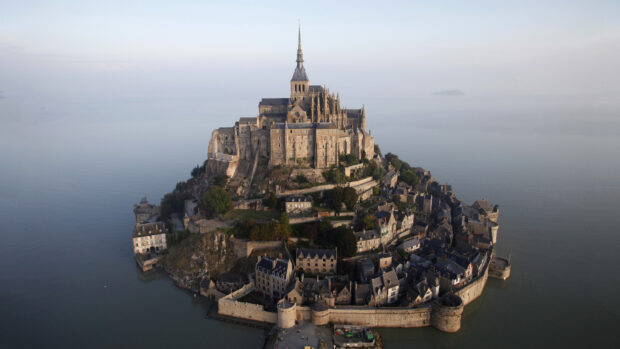 Historic Mont Saint Michel island with medieval architecture surrounded by water at sunrise
