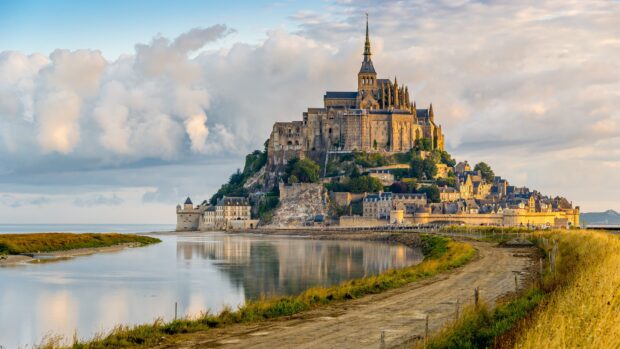 Mont Saint Michel castle surrounded by water and green landscape under cloudy sky