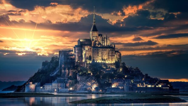 Mont Saint Michel historic island lit up at sunset with dramatic clouds in the background