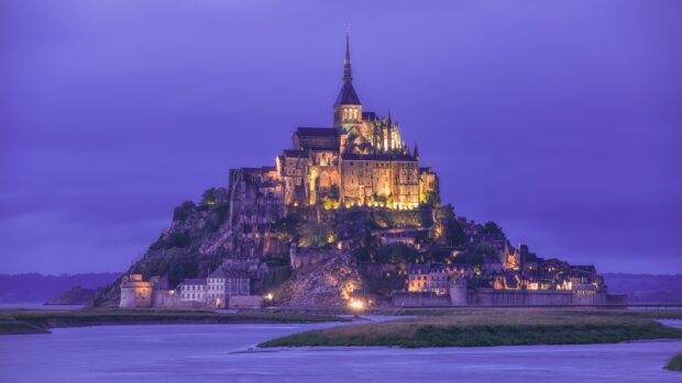 Mont Saint Michel illuminated at dusk with detailed architecture and surrounding water