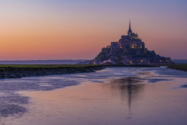 The ancient Mont Saint Michel island with a glowing sunset sky reflected in water