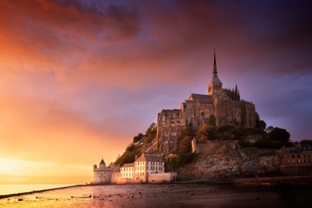 Mont Saint Michel castle and village lit by sunset light under a dramatic sky with Mont Saint Michel in the scene