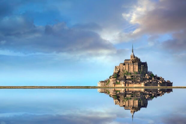 Mont Saint Michel seen clearly with reflection in calm water under a bright sky
