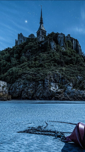 Mont Saint Michel castle surrounded by water and rocks under a starry night sky