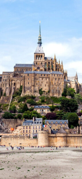 Mont Saint Michel seen from the sandy shore with its historic buildings and towering spire