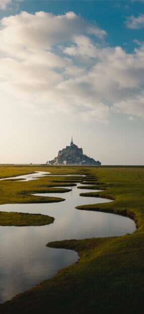 Mont Saint Michel surrounded by grassy marshlands under a cloudy sky