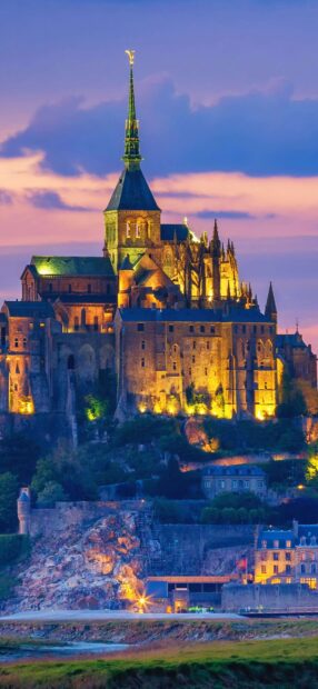 Illuminated Mont Saint Michel at twilight with vibrant sky and historic architecture