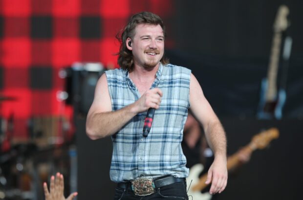 Morgan Wallen wearing a sleeveless plaid shirt performing live on stage at a concert