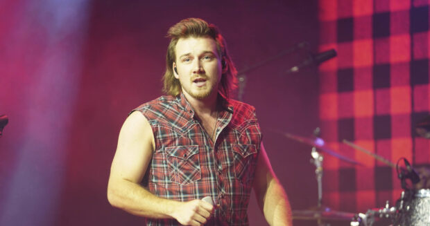 Morgan Wallen wearing a sleeveless plaid shirt singing on stage during a concert