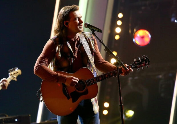 Morgan Wallen playing guitar on stage during a live country music concert