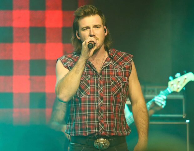 Morgan Wallen singing on stage wearing a sleeveless plaid shirt