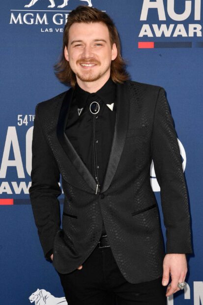 Morgan Wallen wearing a black patterned suit and bolo tie smiling at an awards event