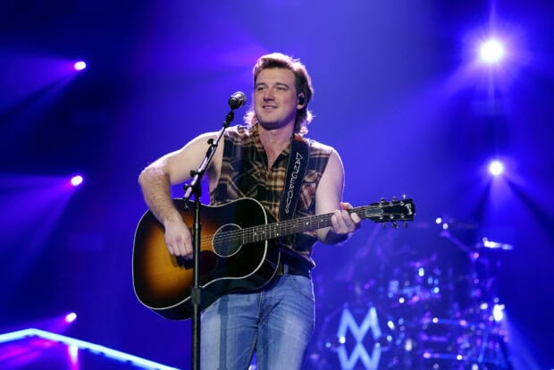 Morgan Wallen performing live with guitar on stage during a concert in a sleeveless plaid shirt
